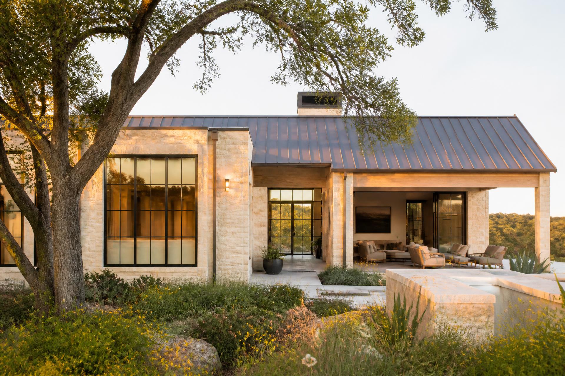 Remodeled Texas Hill Country home with warm limestone walls, a metal roof and native wildflowers at golden hour